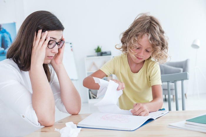 child with anger issues tores out the pages of his notebook , mother sitting beside